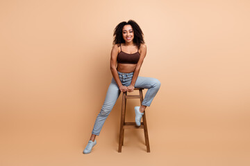 Charming woman sitting on a chair against beige background smiling confidently