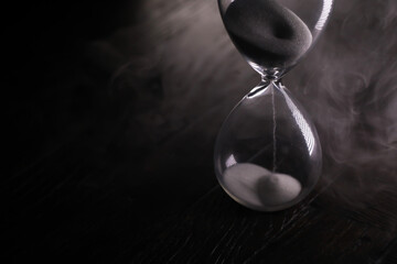 Time Passing Hourglass with Black Sand and Smoky Background in Dim Lighting