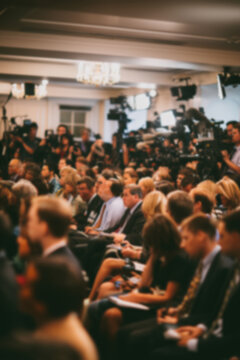 Blurred background image of a crowded press conference room filled with journalists seated and standing, with notepads, cameras, and microphones, all focused on a speaker. News event concept.