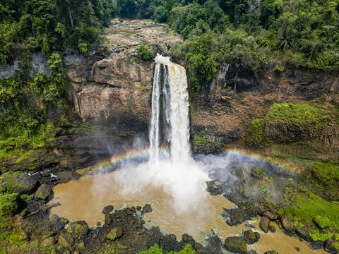 Aerial view of the Ekom-Nkam Waterfalls plunges down a rocky cliff face, a vibrant rainbow arcing across the misty spray, Nkongsamba, Littoral Region, Cameroon.