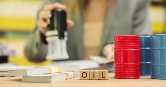 Wooden cubes show word Oil near colorful barrels symbolizing fuel industry and resources shipping. Businesswoman works with paper contract stamping
