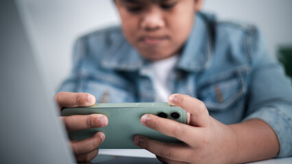 Young person holding green smartphone horizontally, focused on gaming or streaming, with a laptop in foreground, representing digital entertainment and modern youth technology.