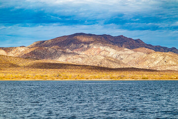 Arid landscape of Mexican coastal shoreline, beach, meadow and mountain range against blue sky, dry and yellowish wild grass, Loreto in Baja California Sur, Mexico