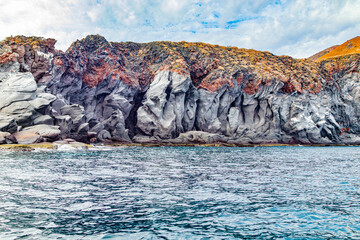 Mexican coastal landscape with rocky mountains on Coronado Island, volcanic lava formations, grayish slope and brown at top, cloudy day in National Marine Park in Baja California Sur, Mexico