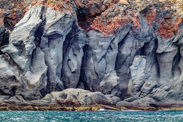 Slope of volcanic lava rock formations on Mexican coast of Coronado Island, sea with blue waters, brown at top, cloudy day in Loreto Bay National Marine Park in Baja California Sur, Mexico