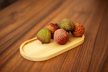 A small wooden oval tray holds a few fresh lychee fruits, some with their outer skin still on, on a...