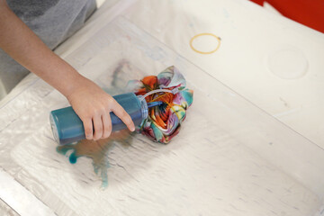 Close-up of a child applying blue dye to a tied fabric in a tie-dye project. Fun and creative...