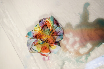 Close-up of a folded tie-dye shirt secured with rubber bands, showcasing vibrant colors and soft...