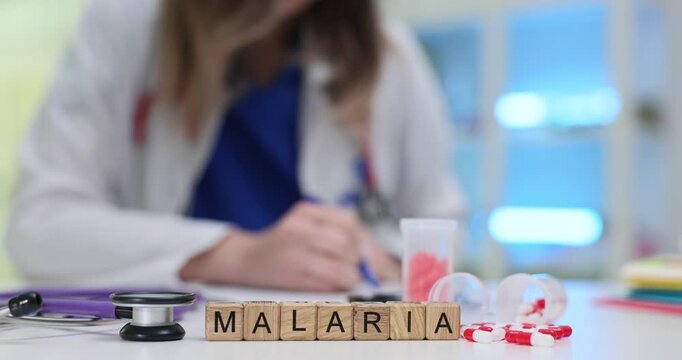 Malaria spelled on cubes brings attention to disease awareness by doctor. Capsules and stethoscope increase association with tropical illness testing