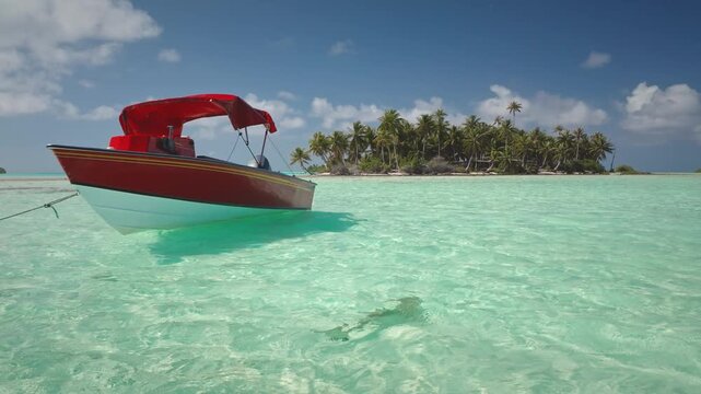 French Polynesia, Rangiroa island: Red and white boat with a bimini top mooring in shallow, crystal clear turquoise water near tropical island, Wild nature travel landscape. Drone flight footage