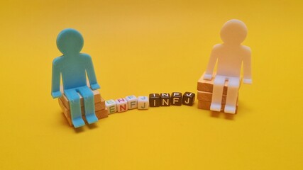 plastic blocks spelling "INFJ" and "ENFJ" with small toy figures, isolated on yellow background. INFJ and ENFJ is 2 of the 16 personality types identified by the Myers-Briggs Type Indicator or MBTI.