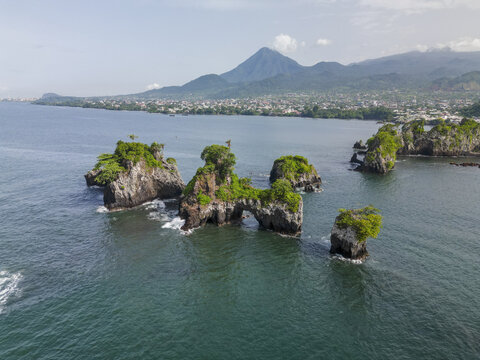 Aerial view of rugged, verdant islets rise from the tranquil sea against the backdrop of a distant mountain and coastal city, Limbe, Southwest Region, Cameroon.