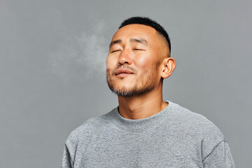 Obraz premium Young Asian Man Exhaling Calm Breath on Light Grey Background for Wellness Ads