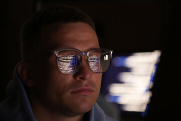 Young man wearing glasses with reflection on dark background, closeup