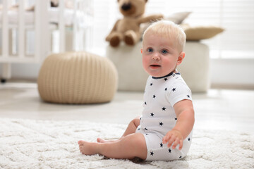 Cute baby sitting on carpet in light room