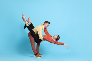 Happy couple in retro outfits dancing on light blue background