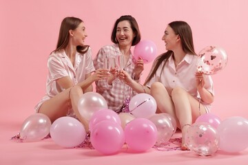 Pajama party. Happy friends with balloons and tinsel clinking glasses on pink background