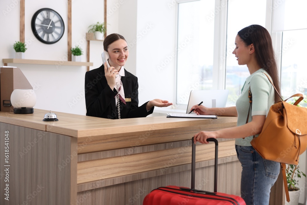 Poster smiling receptionist working with guest at reception desk indoors