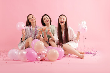 Pajama party. Happy friends with tinsel and balloons clinking glasses on pink background
