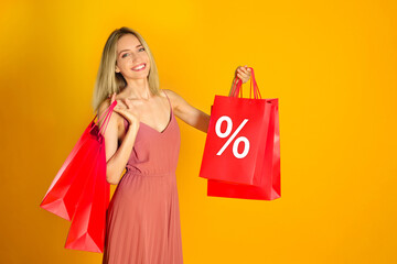 Happy woman with purchases on orange background. Red shopping bag with percent sign. Special offer,...