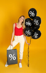 Happy woman with purchase on orange background. Shopping bag and balloons with percent signs....