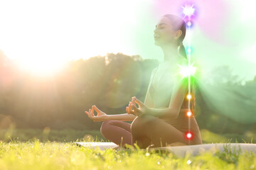 Woman meditating in Lotus pose in nature on sunny morning. Seven chakras glowing