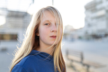 Portrait of blond teen girl looking away with hair covering face in urban setting