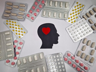 Various blister packs of pills arranged around a head silhouette featuring a red heart inside. Drugs of different shapes and colors for mental wellbeing. Pharmaceutical conceptual background