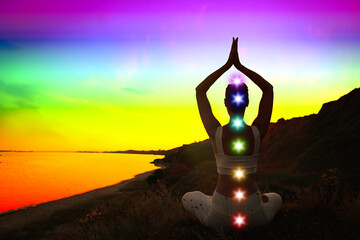 Woman meditating in Lotus pose near sea, toned in rainbow colors. Seven chakras glowing