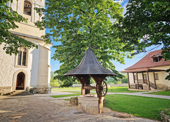 Traditional old well made of wood and stone and the bell tower surrounded by old oak trees inside Capriana Monastery courtyard, Republic of Moldova