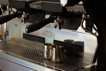 Barista. The pitchers are located under the illuminated coffee machine groups. The background is blurred and has neutral colors