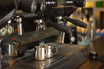 Barista. The pitchers are located under the illuminated coffee machine groups. The background is blurred and has neutral colors