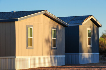 Two manufactured homes with vinyl siding and pitched roofs are displayed on a sales lot, showcasing prefabricated housing models available for purchase