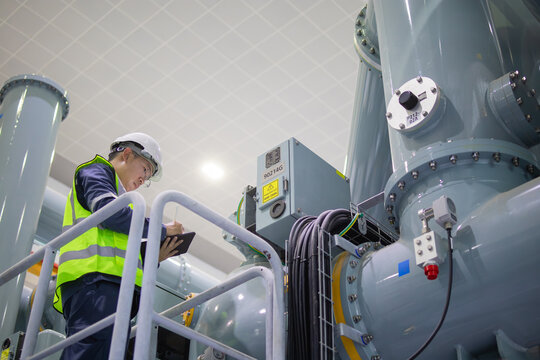 Power station engineer working on industrial equipment with safety helmet and vest in modern facility showing focus and professionalism in maintenance and inspection tasks