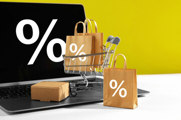 Hot sale, special offer. Shopping cart, purchases and laptop against yellow background. Percent...