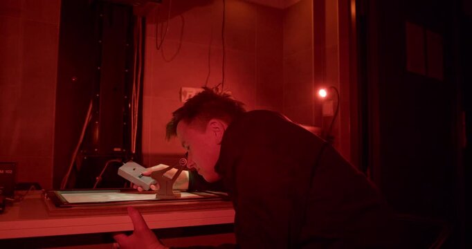 Checking for critical sharpness in a photographic darkroom. A printer uses a grain focuser on an enlarger easel to examine the projected image's grain, ensuring the final print will be perfectly sharp