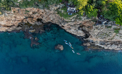 Aerial View of Paddleboarders Exploring Crystal Clear Cove by Rocky Cliffs