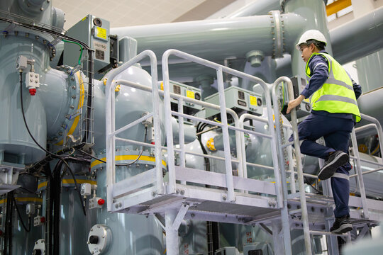 Power station engineer inspect industrial equipment climbing metal stairs wearing safety helmet and reflective vest in factory environment