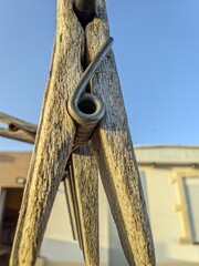 Weathered wooden clothespin with metal spring against a bright blue sky