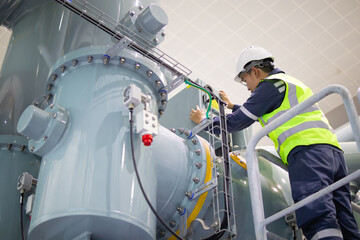 Gas insulated switchgear inspection in substation shows technician wearing safety helmet and vest...
