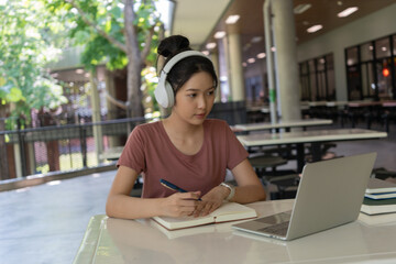 Young Asian student studying independently outside classroom. Learning from books and smartphone in a relaxed environment. Modern education, self-study, and digital lifestyle.