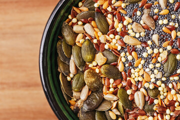 Healthy omega seed mix background. Assortment of seeds in black ceramic bowl on wooden table. Pumpkin chia flax millet sunflower seeds mix. Superfood nutrition concept for healthy lifestyle.