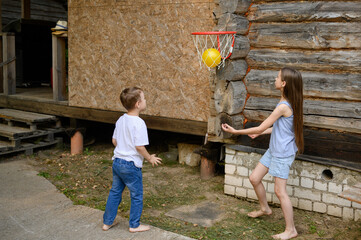 Brother and sister play with ball on summer day running barefoot in backyard of house, throwing...