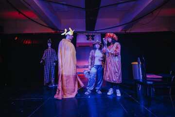 Actors wearing costumes perform a theatrical play on a brightly lit stage, showcasing drama and...