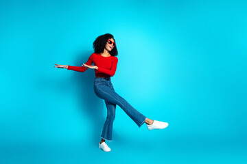 Young attractive woman in trendy casual wear dancing joyfully against a bright blue background with...