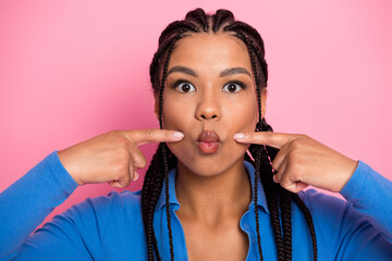 Attractive young woman in a blue casual top against a pink background with a playful expression and...