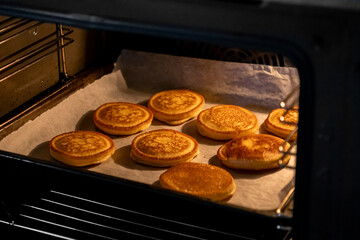 Delicious homemade golden pancakes baking on parchment paper inside a warm oven, representing comfort food, cozy breakfast, or a sweet dessert treat