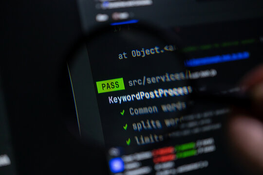 Magnifying glass highlighting programming code with a PASS message on a dark screen, symbolizing successful software development or quality assurance