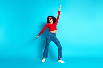 Stylish young woman in red top and blue jeans posing against vibrant blue background expressing cheerful gestures