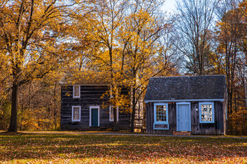 Rustic wooden cabins surrounded by vibrant autumn foliage in a peaceful countryside setting, bathed in warm fall sunlight.